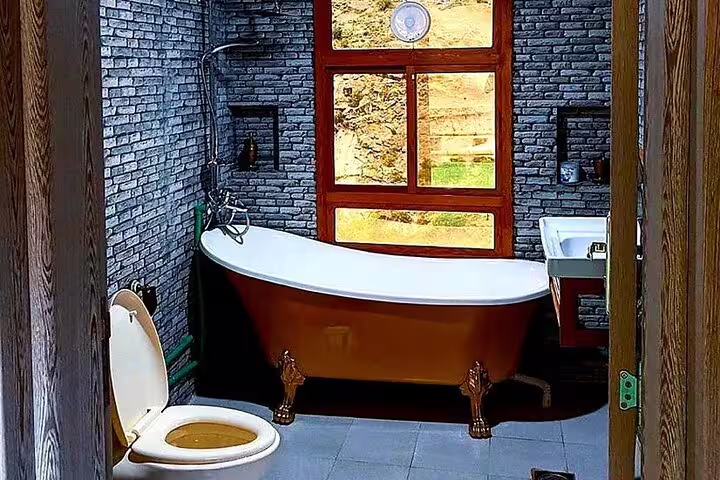 Rustic bathroom with clawfoot tub and brick walls in Jebel Akhdar Al Suwjara Village tour accommodation.