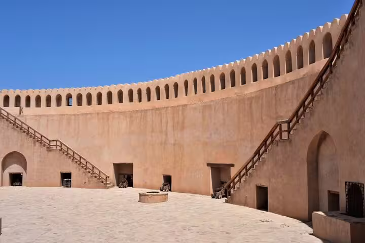 Inside view of an ancient fort with high walls and stairs, under a clear blue sky at Jebel Shams, ideal for exploration.