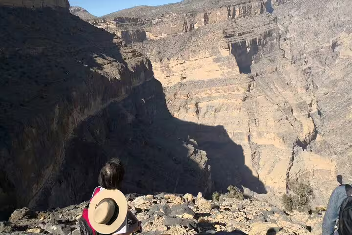 A hiker sits at the edge, admiring the breathtaking canyon views at Jebel Shams during a full-day guided tour.