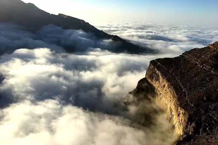 Clouds blanket the valleys of Jebel Shams, creating a stunning above-the-clouds experience on a guided hiking tour.