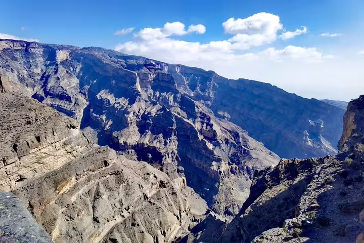 Majestic panoramic view of Jebel Shams' rugged cliffs under a bright blue sky, perfect for a scenic hiking adventure.
