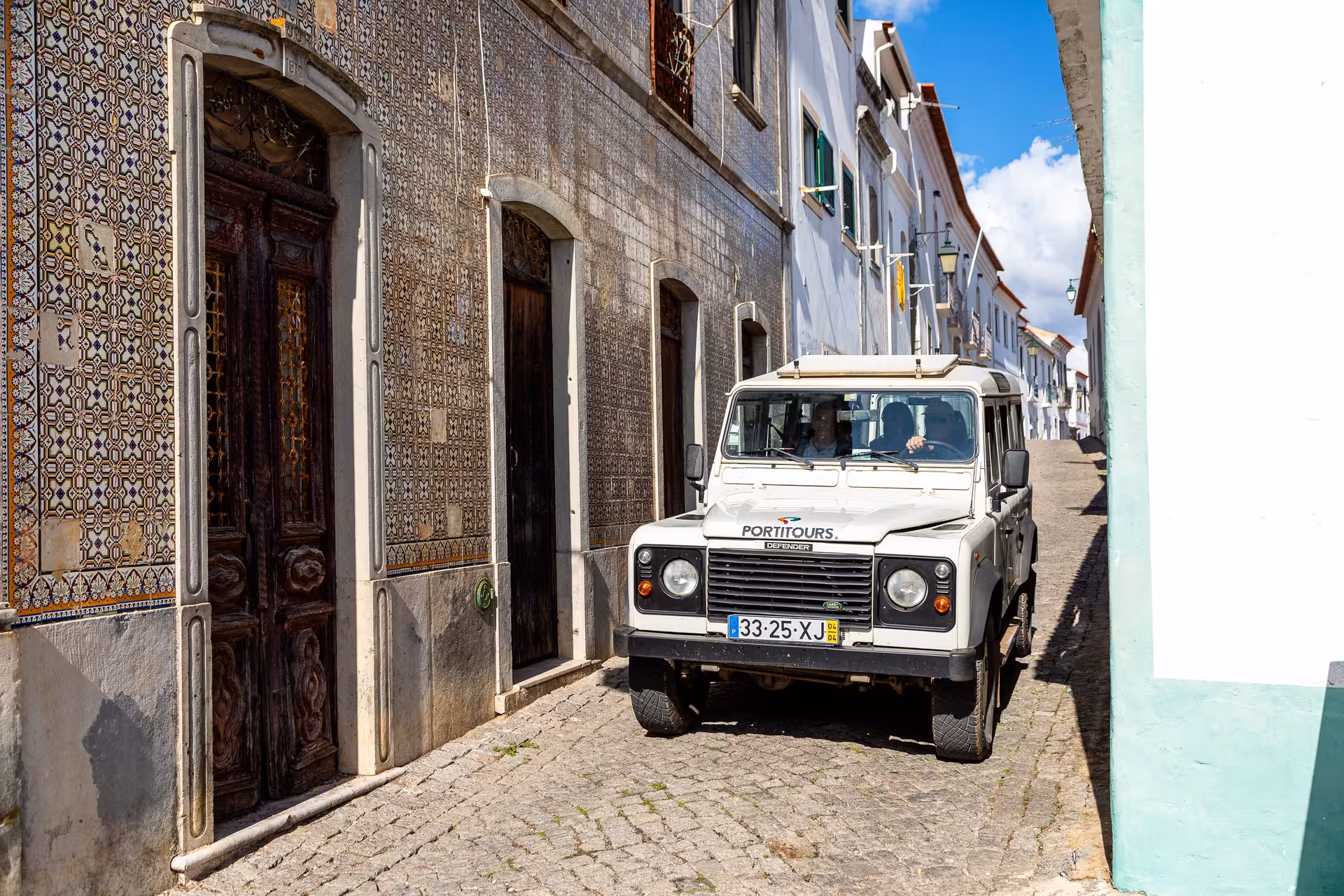 4x4 jeep safari in Algarve driving through narrow cobbled village street lined with tiled Portuguese houses and blue sky