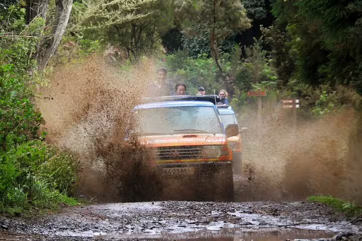 Jeep splashes through muddy terrain on the Wine & Cabo Girão Safari tour, showcasing Madeira's lush landscapes and adventure.