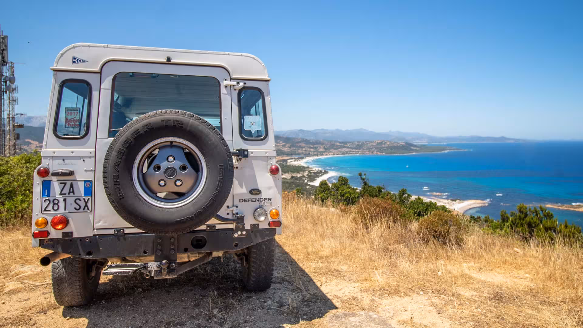 4x4 Jeep overlooking stunning coastal landscape of Capo Comino, Sardinia, highlighting the turquoise sea and rugged terrain.