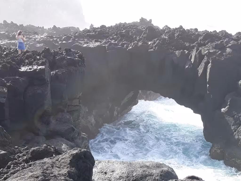 Traveler exploring rugged lava cliffs and natural ocean arch near Ferraria on a full-day Jeep tour from Ponta Delgada