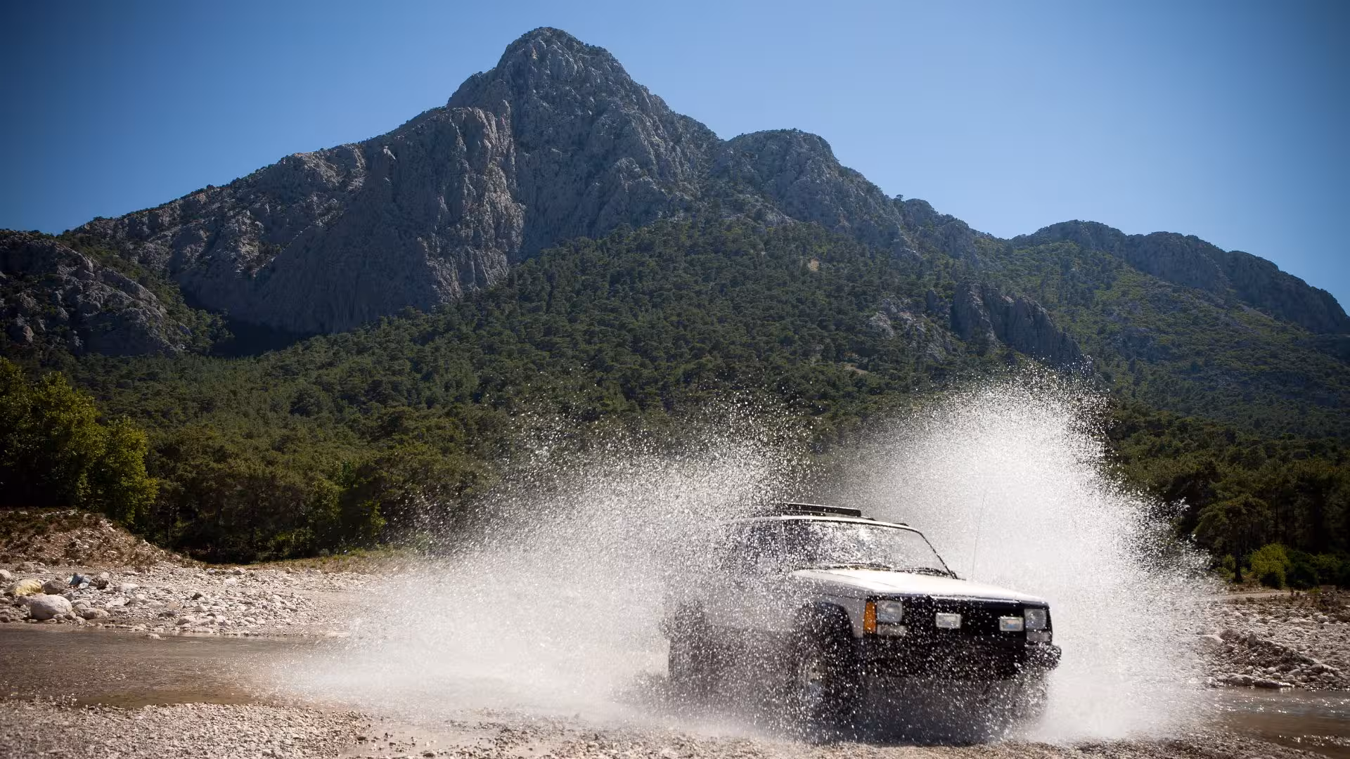 Jeep splashing through water with Supramonte mountains in the background on a sunny day.