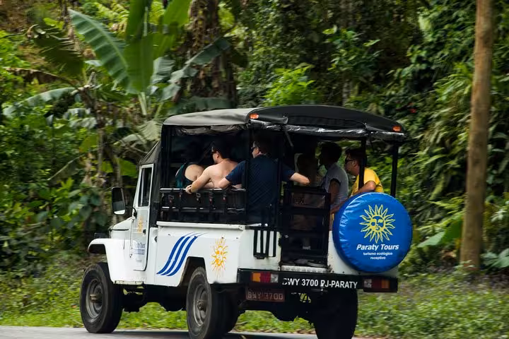 Open-air Jeep filled with tourists exploring lush rainforest on an exhilarating Jeep Tour to waterfalls.