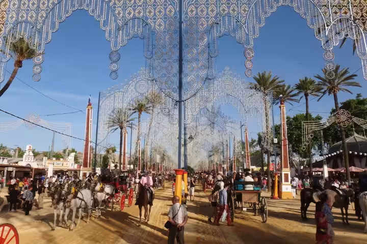 Festive scene at the Jerez Horse Festival, featuring vibrant decorations, horse-drawn carriages, and lively crowds under sunny skies.