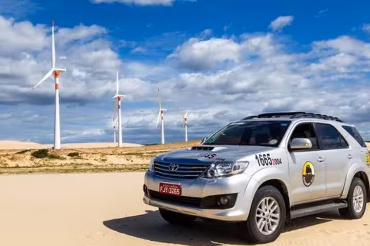 Silver Toyota 4x4 SUV parked on sandy dunes near wind turbines during Jericoacoara to airport transfer