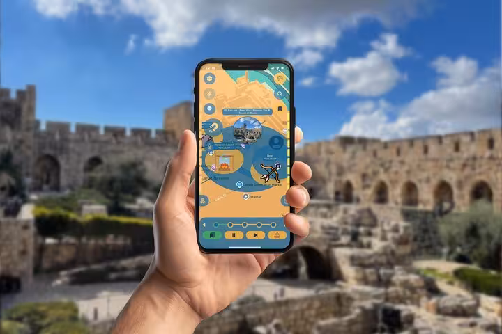 Hand holding smartphone with Jerusalem self-guided tour app, ancient city walls in background
