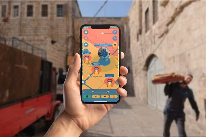 Hand holding smartphone with Jerusalem self-guided walking tour game app in ancient stone alleyway