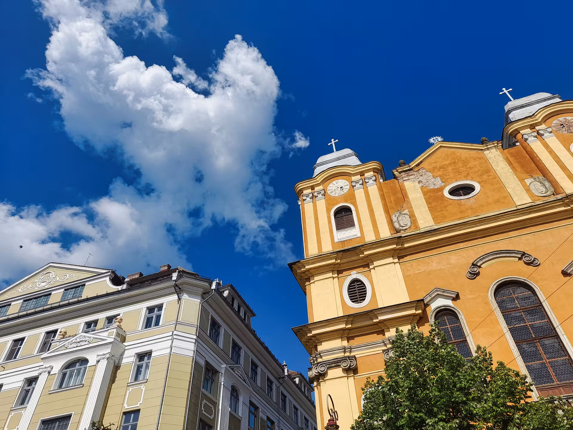 Stunning upward view of the baroque Jesuit Church golden facade and twin towers against a vivid blue sky on a Cluj-Napoca history walking tour.