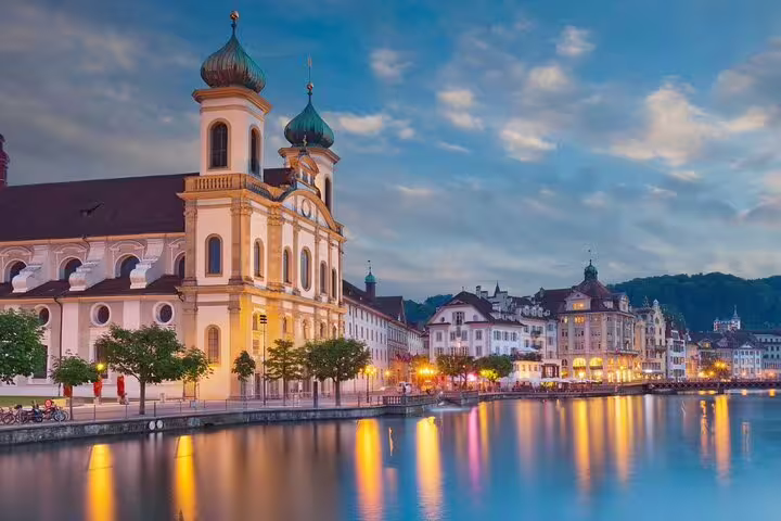 Picturesque view of Jesuit Church reflecting on Reuss River at twilight in Lucerne, perfect for Engelberg excursions.