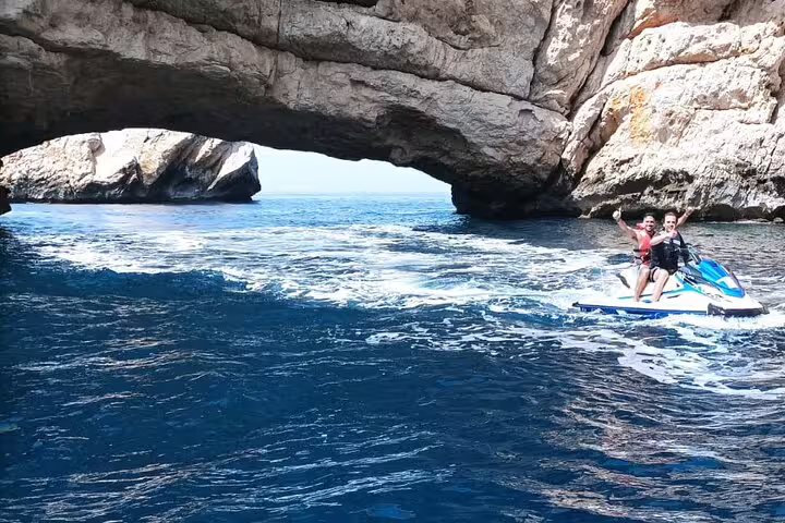 Riders on jet ski passing under sea arch near Portitxol, Javea, on guided Costa Blanca excursion