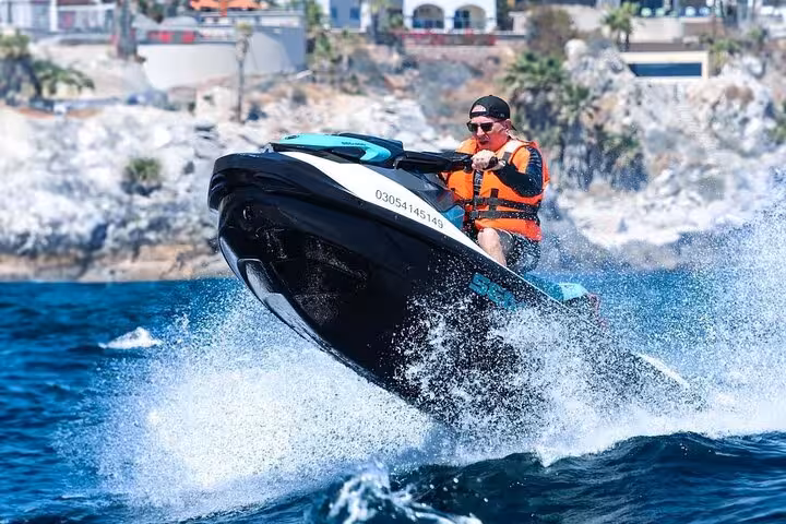 Man riding jet ski on blue ocean waters near rocky coastline wearing orange life jacket