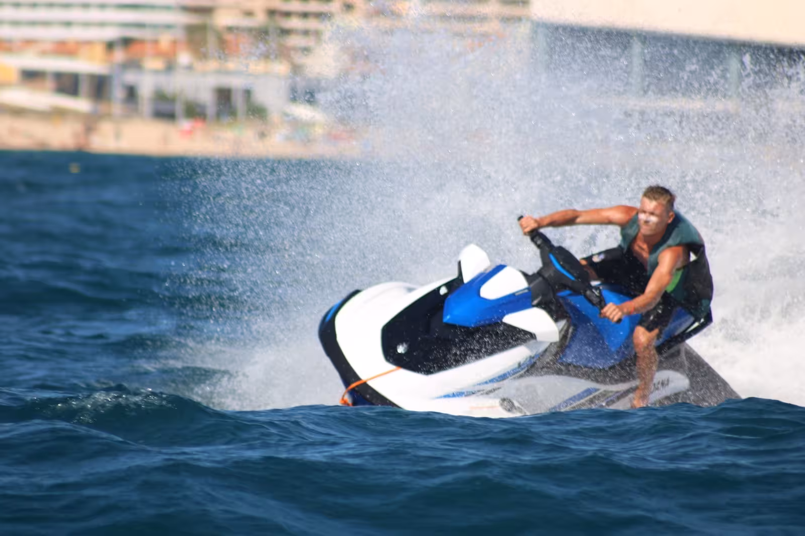Adventurous rider carving sharp turn on blue jet ski at Praia da Rocha Baixinha, Algarve high-speed water sports