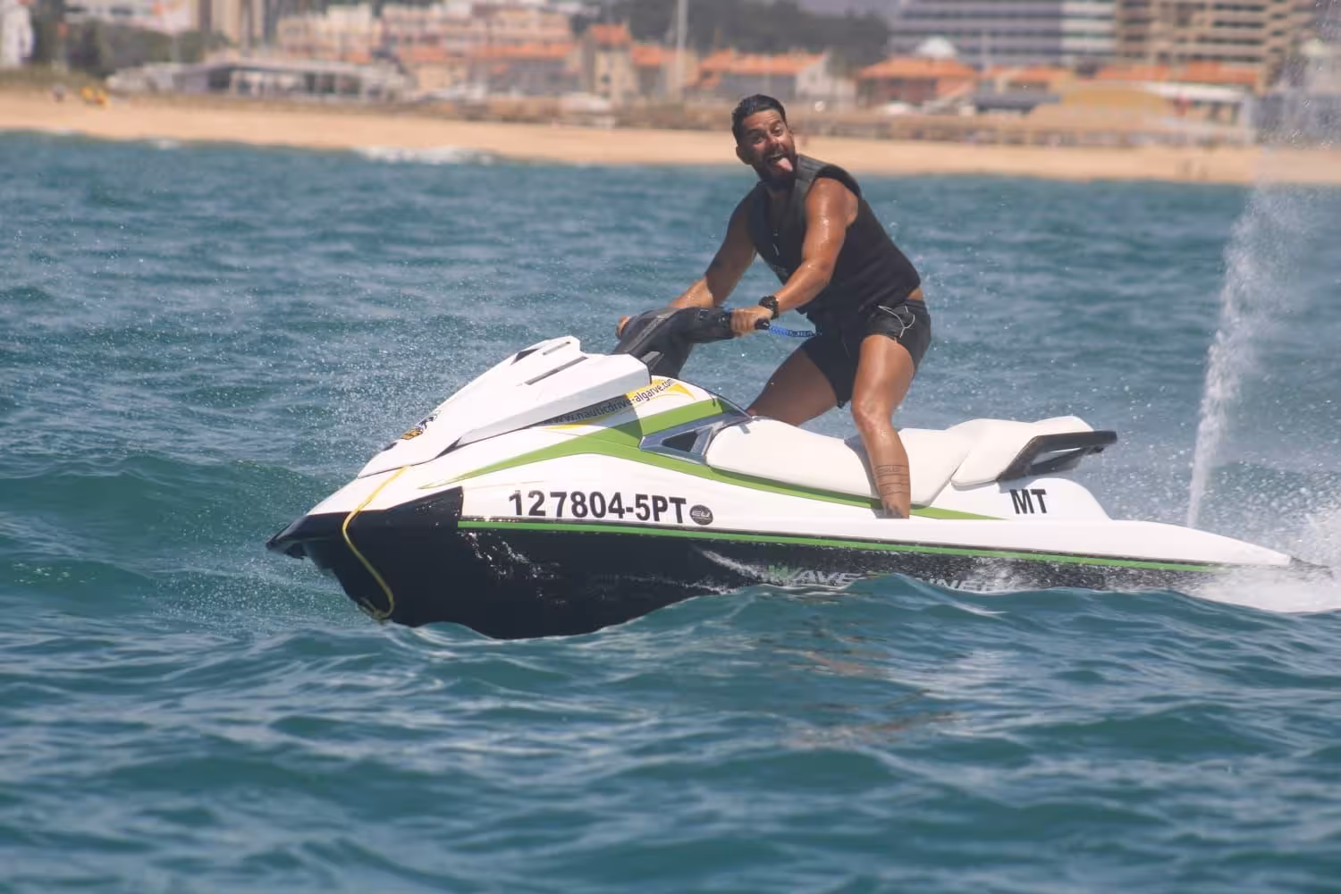 Excited man riding a white jet ski off Praia da Rocha Baixinha, splashing through Algarve’s blue Atlantic water