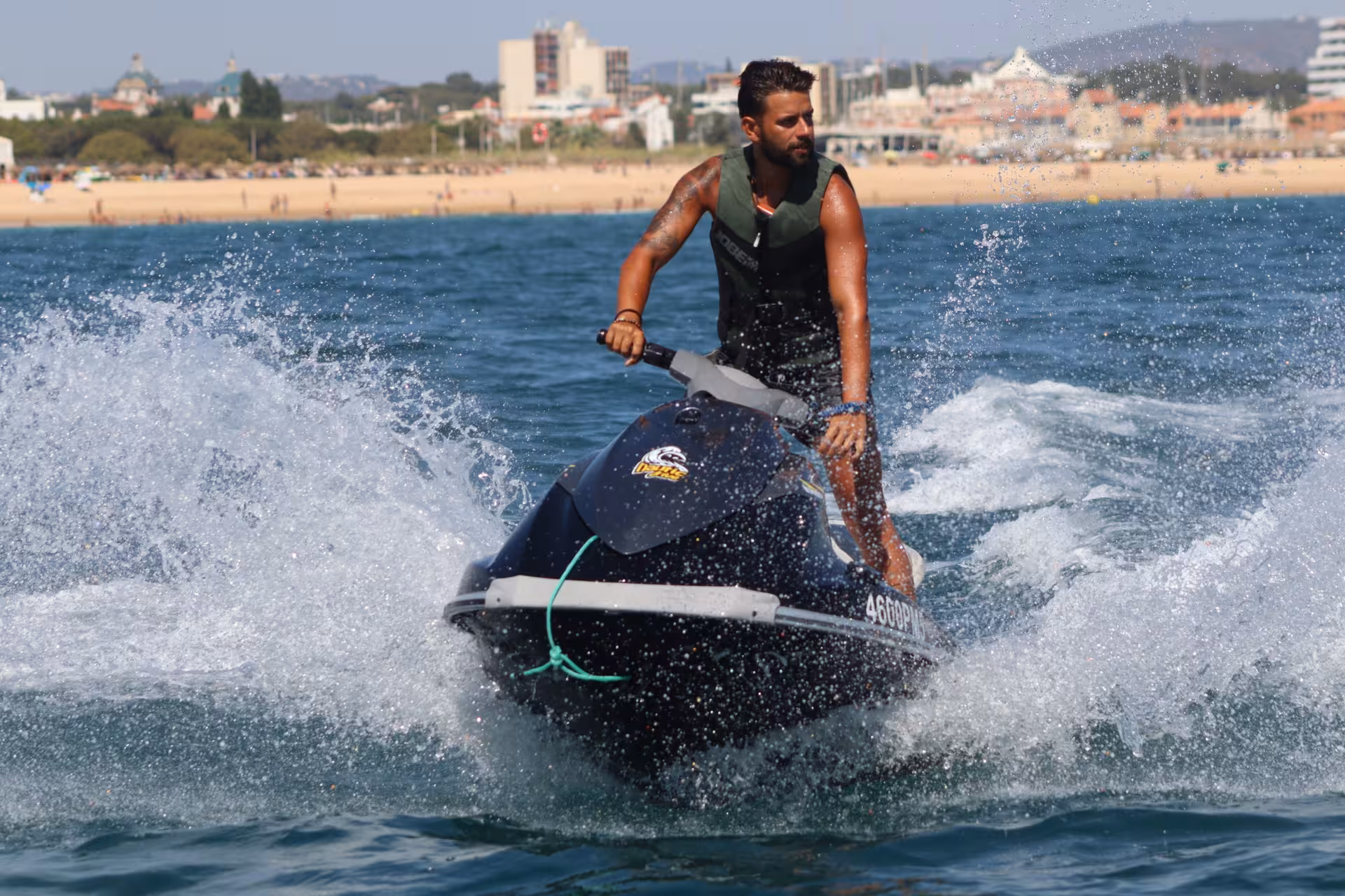 Jet ski rider speeding past Praia da Rocha Baixinha beach with Albufeira skyline in the background on a sunny Algarve day
