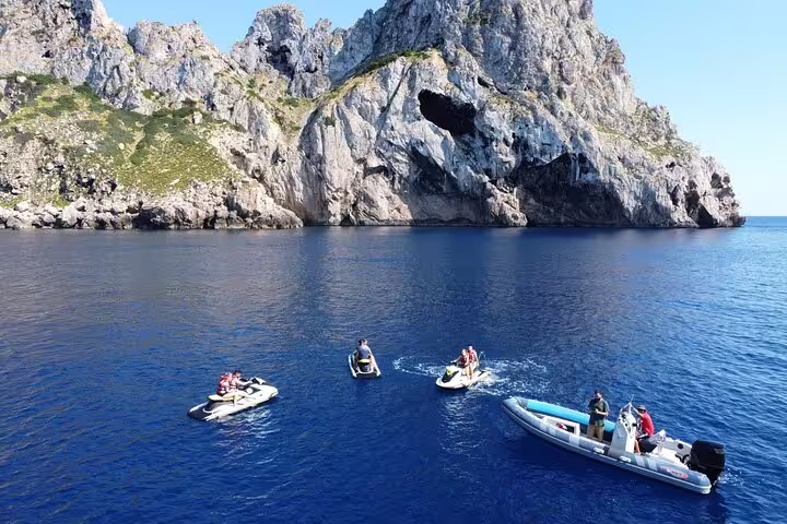 Jet ski group and support boat on the San Antonio Ibiza to Es Vedrá tour, cruising past dramatic rocky coastline