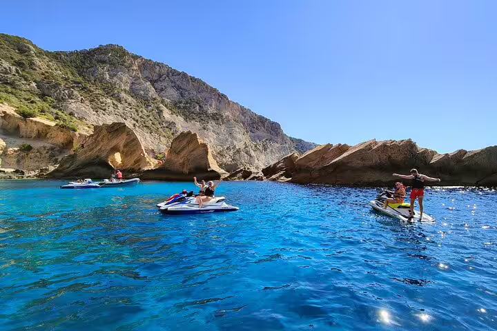 Group jet ski tour from San Antonio Ibiza to Atlantis, cruising in crystal-clear bays below rocky cliffs