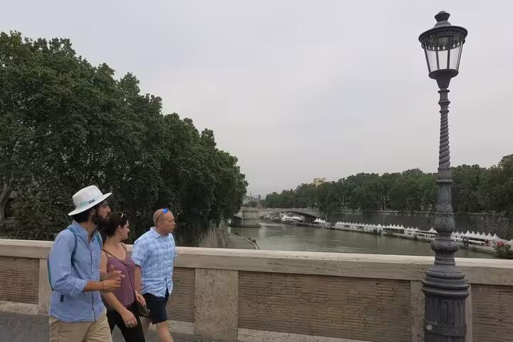 Tourists walking along the Tiber River in Rome's Jewish Ghetto, exploring historical sites and culinary heritage.