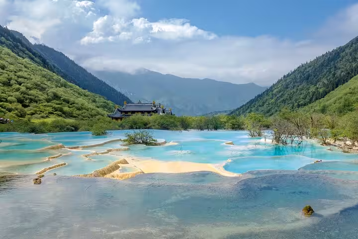 Scenic view of Jiuzhaigou's turquoise terraced pools surrounded by lush mountains on a sunny day.