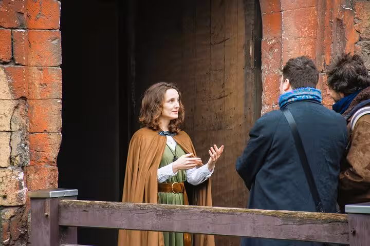 Medieval costumed guide in green dress and brown cape speaking to visitors at historic stone building in Rouen