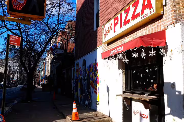 Joe's Pizza storefront since 1975 with red awning and street art mural in Williamsburg Brooklyn