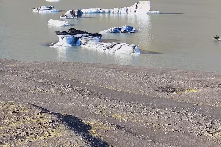 Icebergs floating on the glacial lagoon at Jokulsarlon with dark volcanic sand shore in Iceland