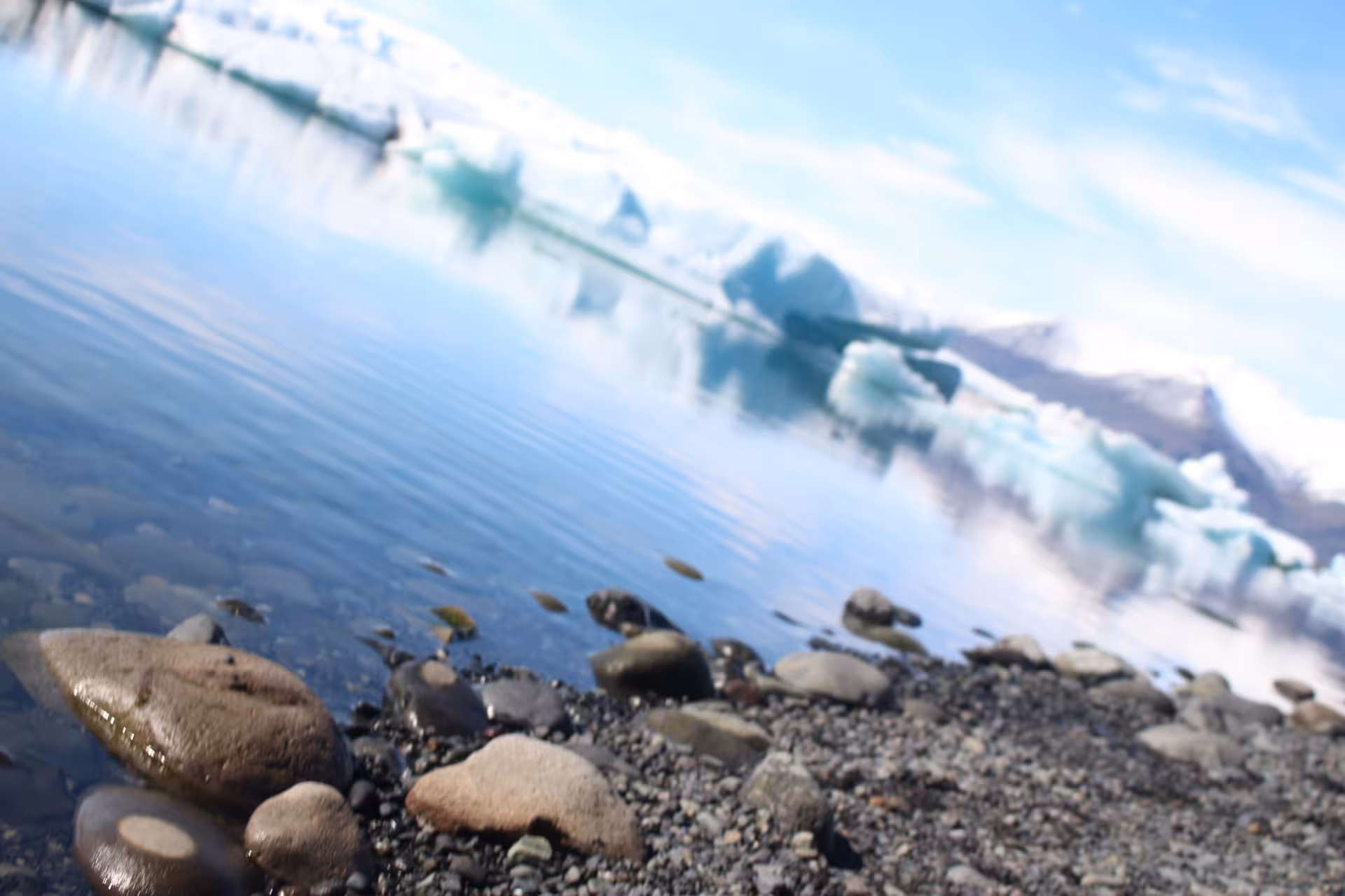 Rocky shoreline with floating icebergs on Jokulsarlon glacial lagoon under blue sky