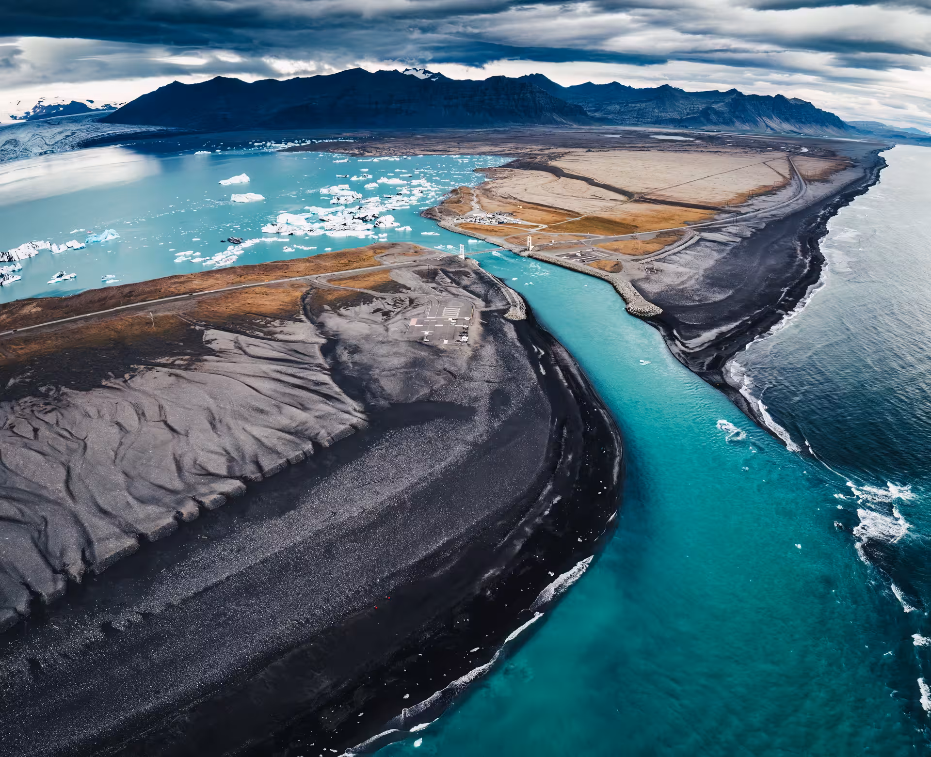 Aerial view of Jokulsarlon Glacier Lagoon with turquoise glacial river channel meeting the Atlantic Ocean on Iceland's black sand coast