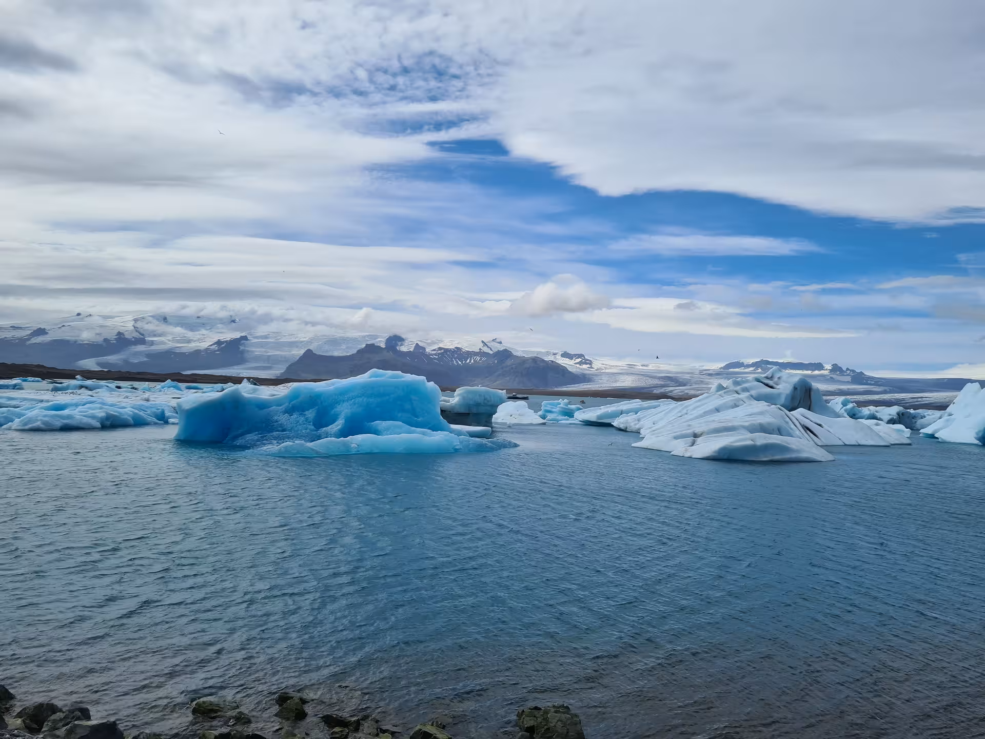 Blue icebergs floating in Jokulsarlon glacier lagoon with snow-capped mountains in Iceland