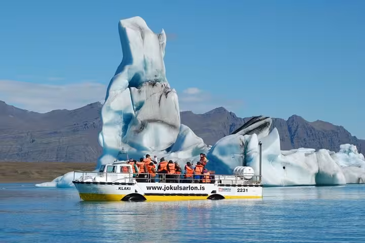 Tour boat with passengers in orange life jackets navigating among icebergs at Jokulsarlon Glacier Lagoon, Iceland