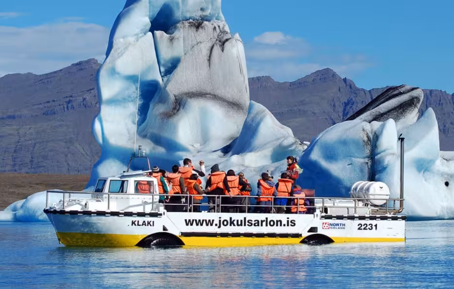Tourists in orange life jackets on Jokulsarlon glacier lagoon boat tour near massive iceberg, Iceland