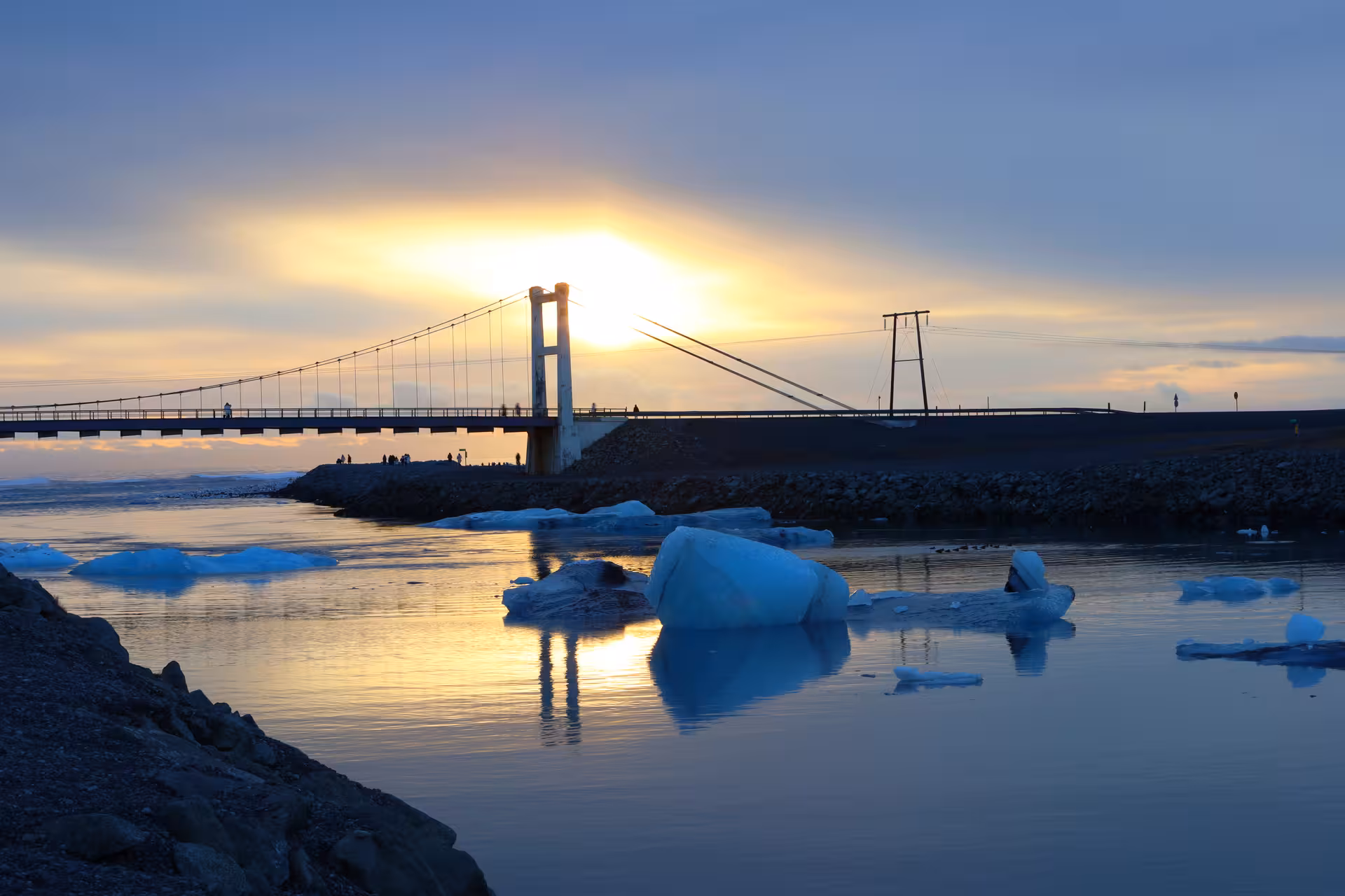 Jökulsárlón glacier lagoon with floating icebergs and suspension bridge at golden sunset, Iceland South Coast
