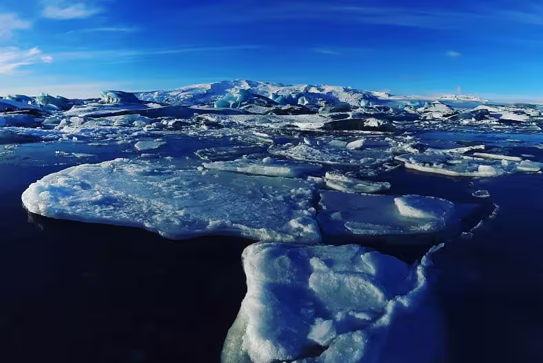 Floating ice chunks on dark waters at Jokulsarlon Glacier Lagoon, Iceland, under a bright blue sky