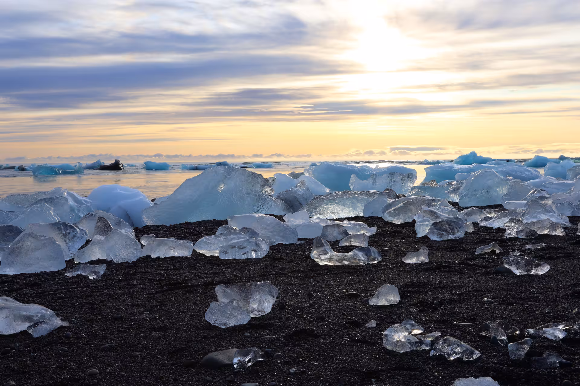 Ice chunks on black volcanic sand beach at Jokulsarlon glacier lagoon during golden sunset, Iceland