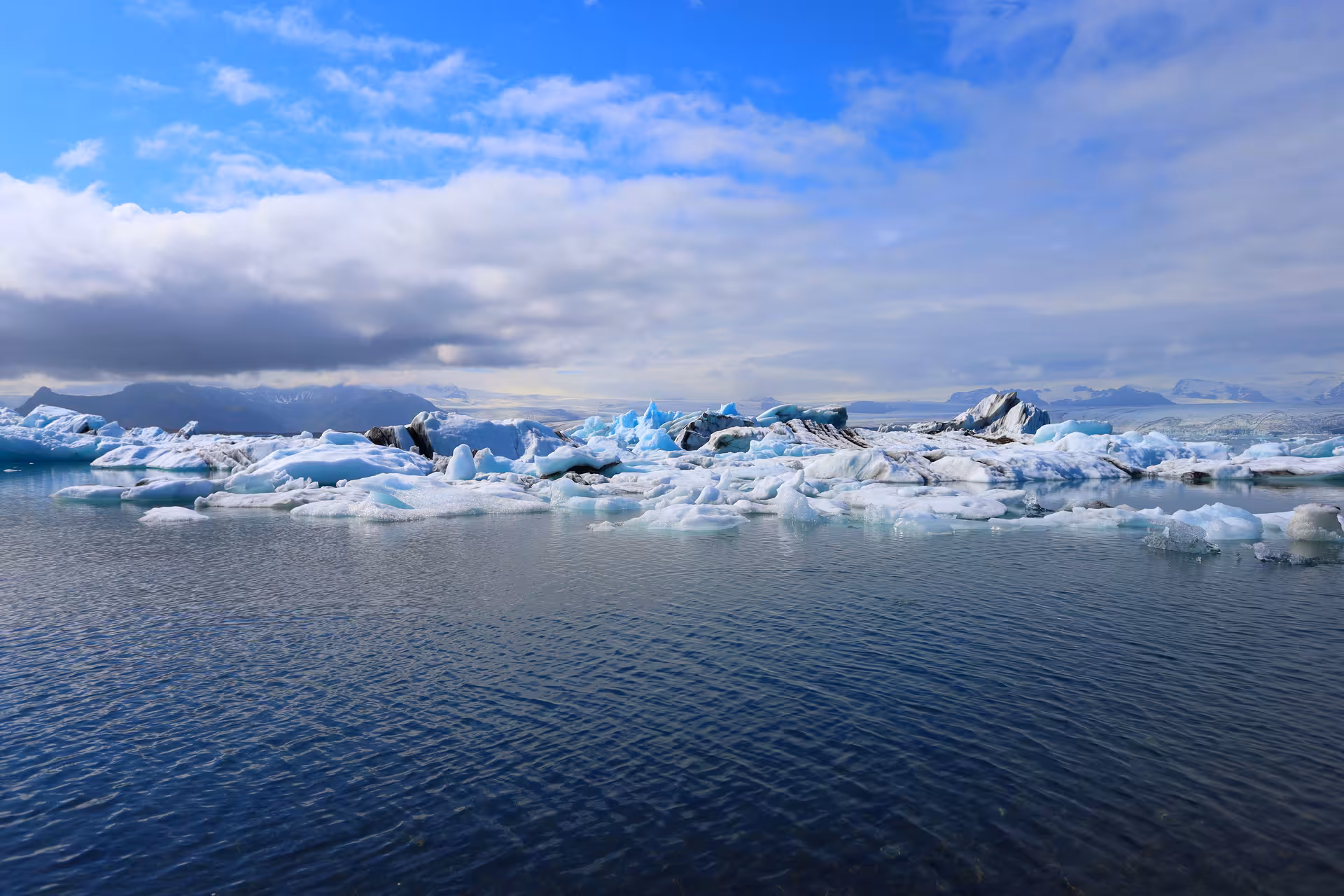Floating icebergs on Jokulsarlon glacial lagoon with blue sky and mountains in Iceland