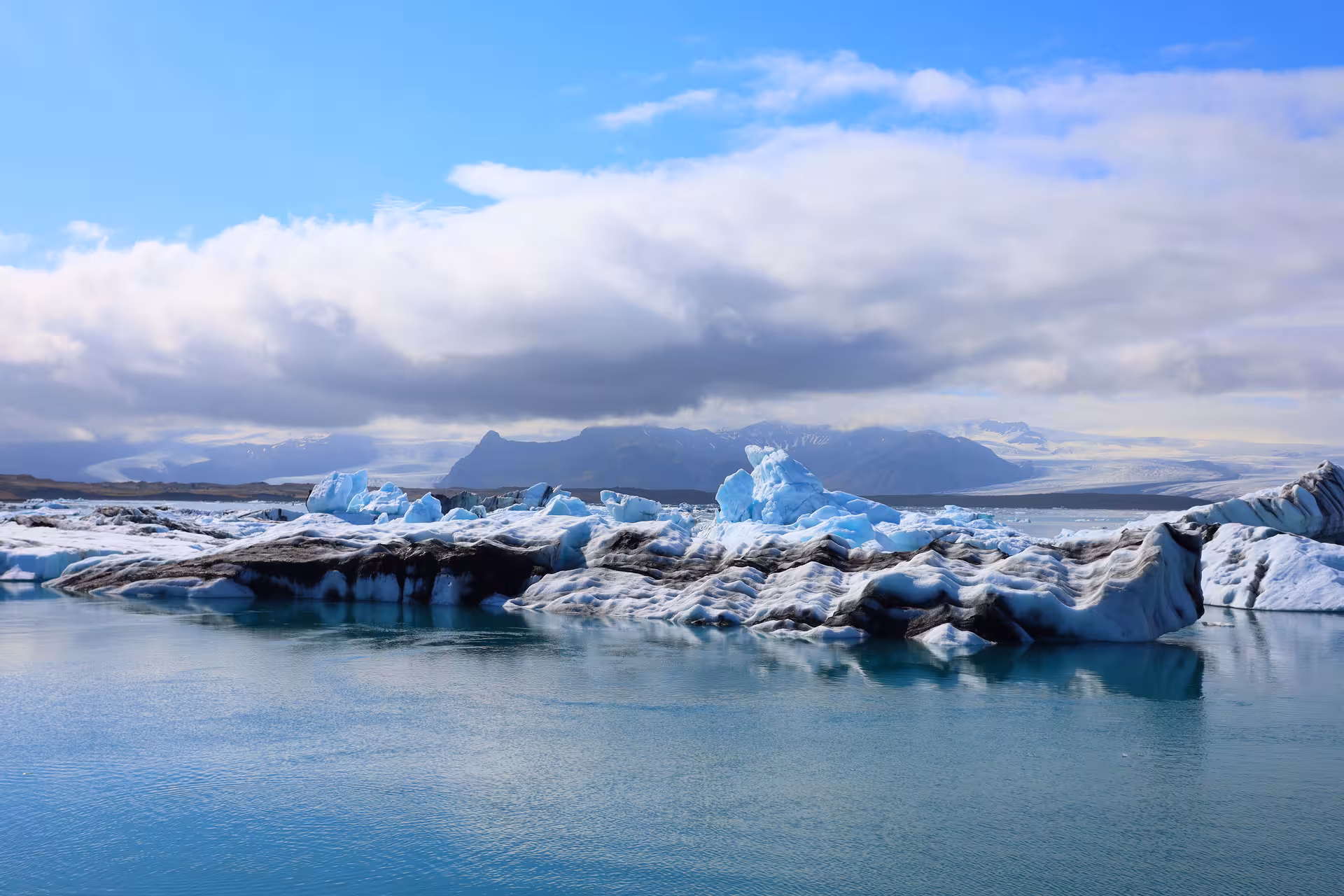 Icebergs floating on Jokulsarlon glacier lagoon with snow-capped mountains and blue sky in Iceland