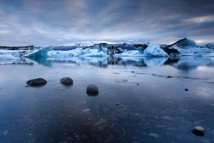 Icebergs and dark volcanic rocks reflected in the still waters of Jokulsarlon Glacier Lagoon, Iceland