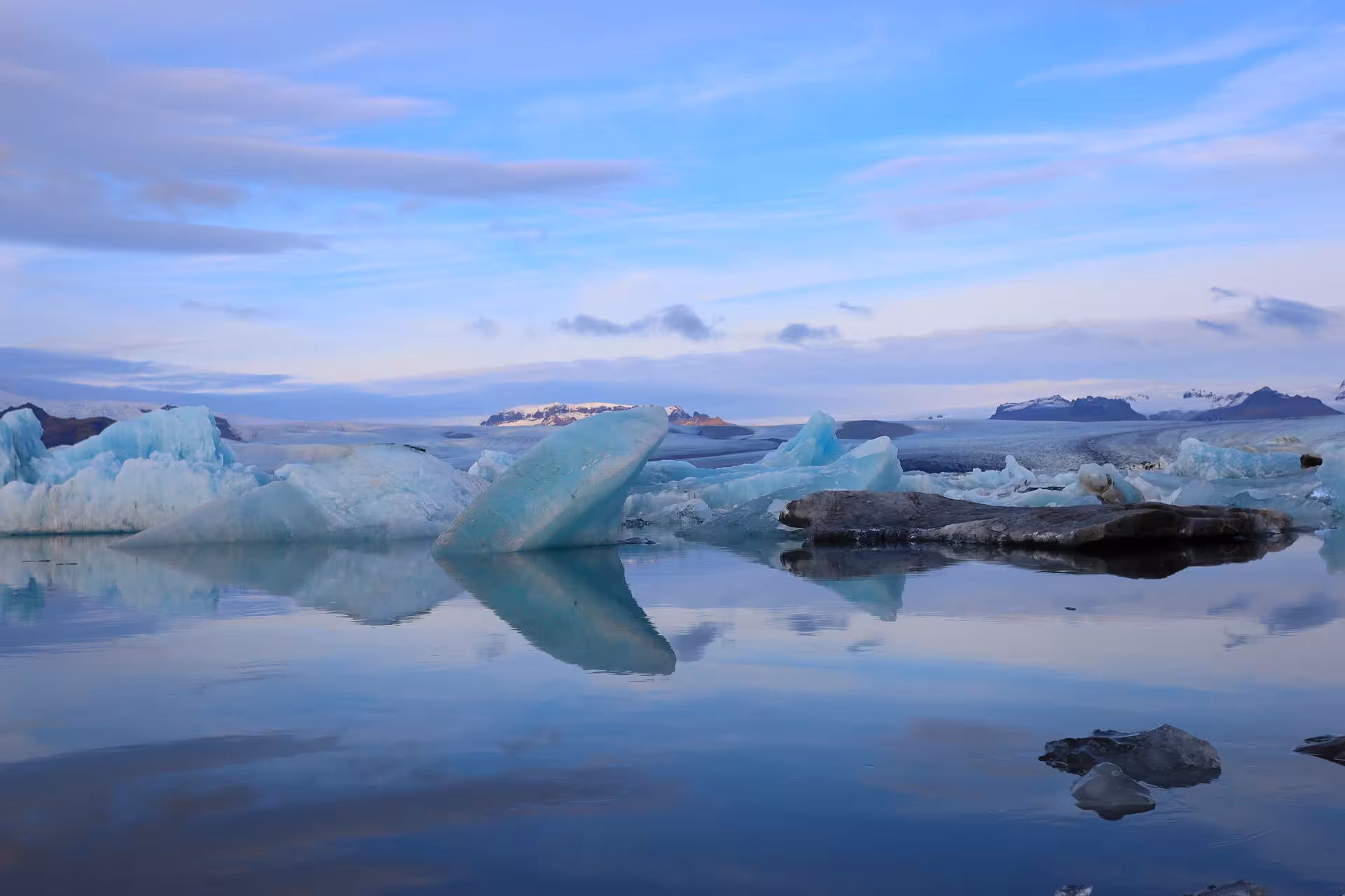 Turquoise icebergs floating on calm glacial lagoon with snow-capped mountains in Iceland