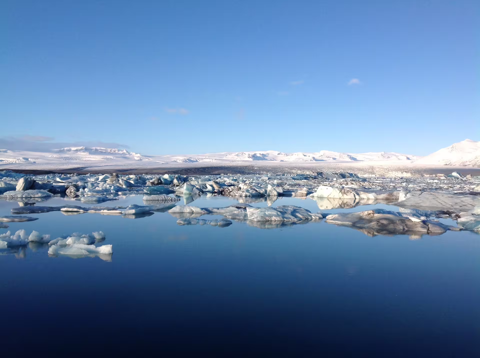 Icebergs floating on the still blue waters of Jökulsárlón Glacier Lagoon, Iceland, with snow-covered mountains in the background