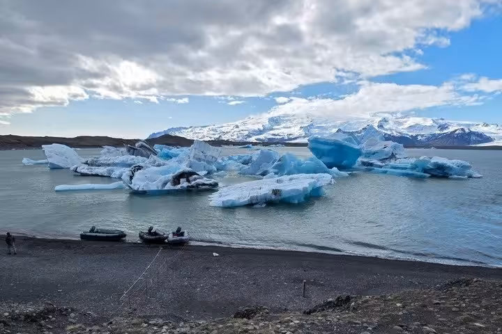 Blue icebergs floating in Jokulsarlon glacier lagoon with snow-capped mountains and black sand beach shore