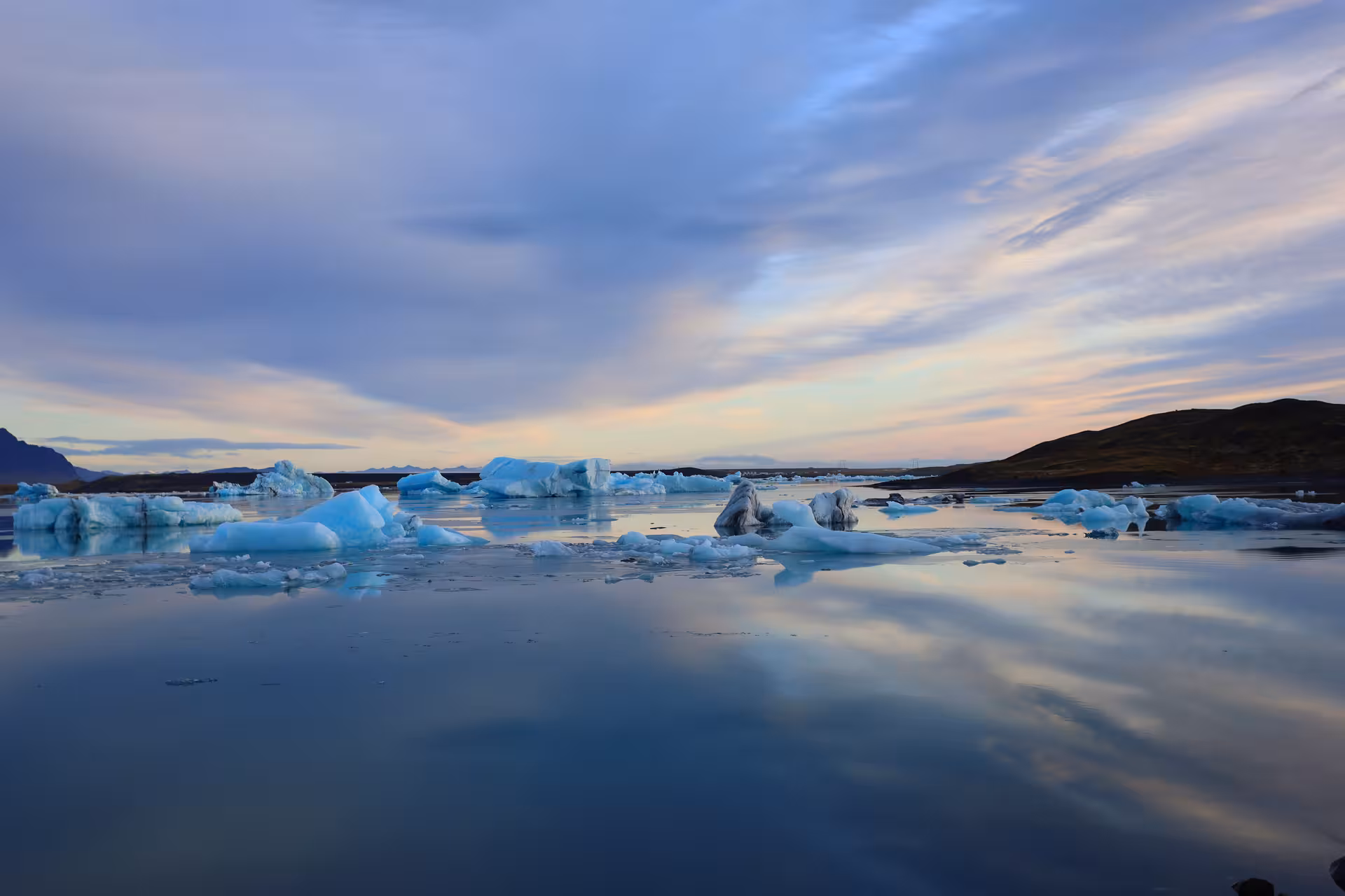 Floating icebergs on calm reflective waters of Jokulsarlon Glacier Lagoon at sunset, Iceland