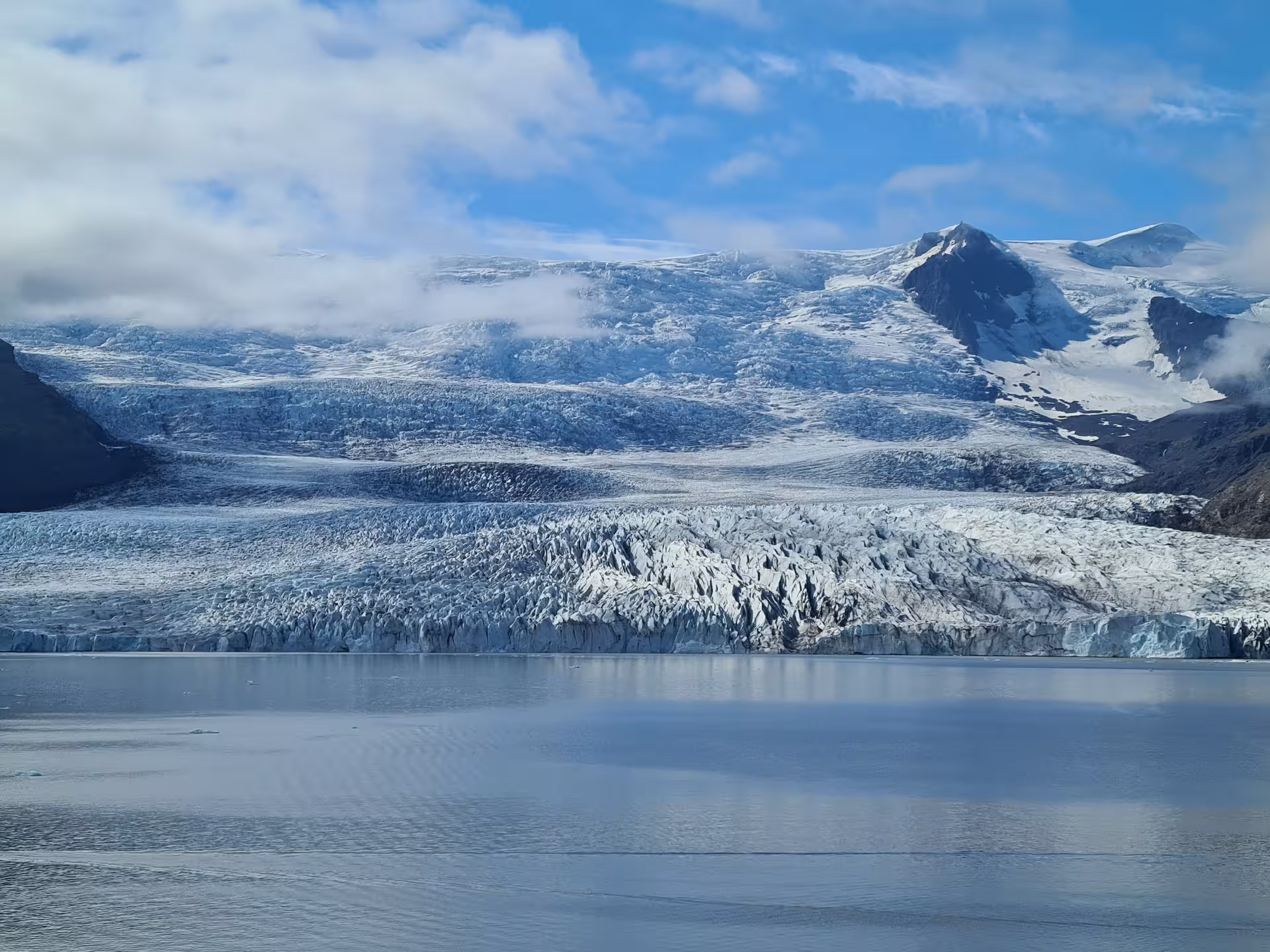 Massive glacier calving into Jokulsarlon glacial lagoon with jagged ice formations and snow-capped mountains, Iceland