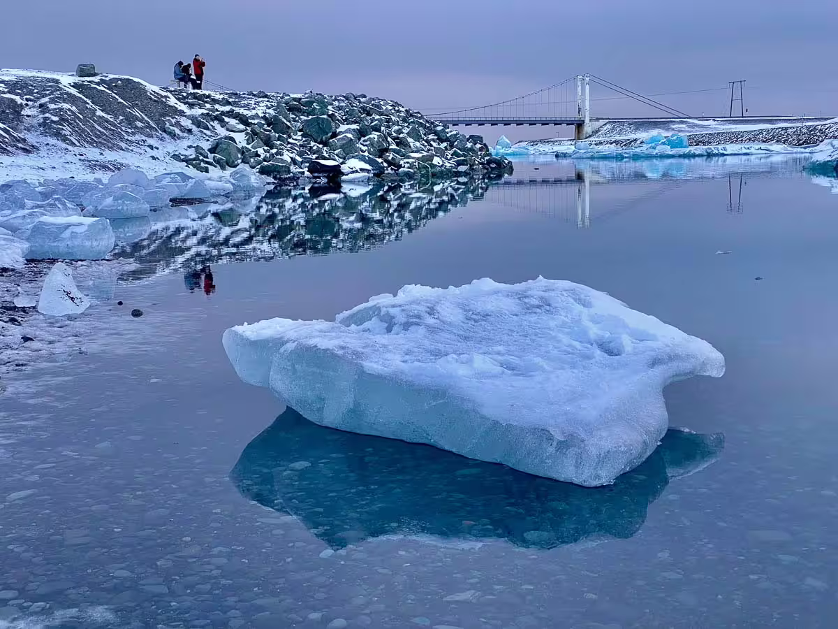 Floating iceberg on Jökulsárlón glacier lagoon with suspension bridge and tourists on rocky shore, Iceland