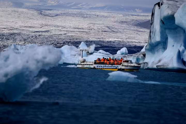 Tour boat with passengers in orange jackets navigating icebergs at Jokulsarlon Glacier Lagoon Iceland