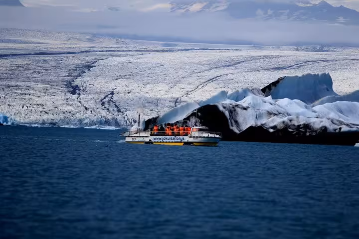 Tour boat with passengers in red life jackets navigating Jokulsarlon glacier lagoon Iceland