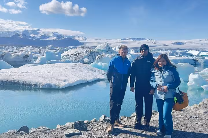 Three tourists posing at Jokulsarlon Glacier Lagoon with floating icebergs and turquoise water in Iceland