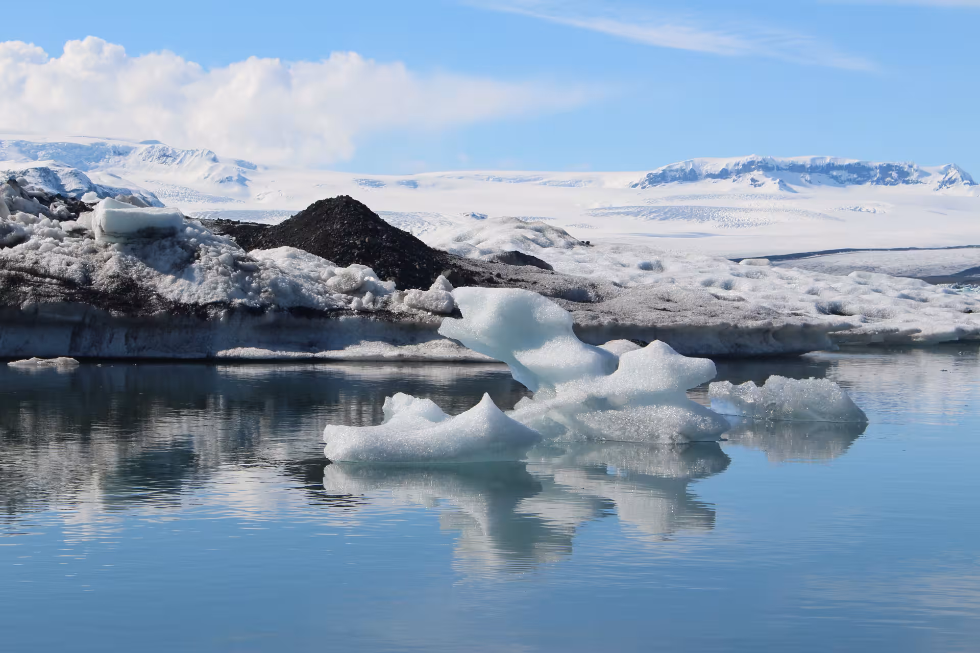 Floating icebergs on the calm glacial waters of Jokulsarlon Lagoon with snow-covered glacier and mountains behind